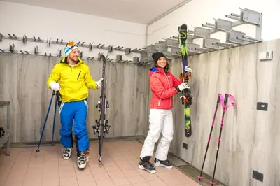 two people are standing in a room with skis at Hotel Villa Rosella Park & Wellness in Canazei