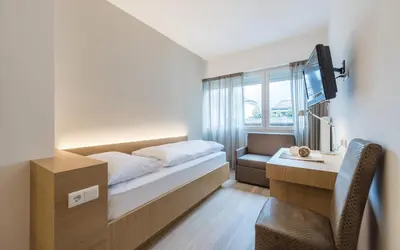 a bedroom with a bed and a desk and a tv at Hotel Post Gries in Bolzano