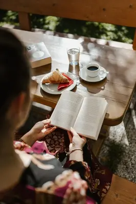 a woman sitting at a table reading a book at Pension Siller in Lagundo