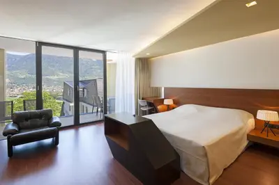 a bedroom with a bed and a chair and a large window at Parkhotel Marlena - Adults Only in Merano