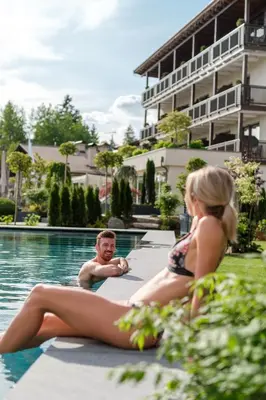 a man and a woman sitting next to a swimming pool at Hotel Salten in Avelengo