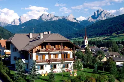 a house in a village with mountains in the background at Hotel Garní Sunnleit´n in Monguelfo