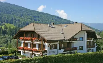 a house on a hill with a mountain in the background at Hotel Garní Sunnleit´n in Monguelfo