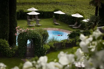 a pool with umbrellas and chairs and a person swimming at Hotel Magdalener Hof in Bolzano
