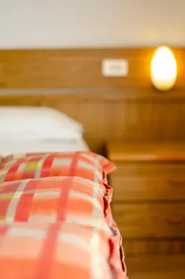a close up of a bed with a pillow and a night stand at Hotel Cristallo in Vigo di Fassa