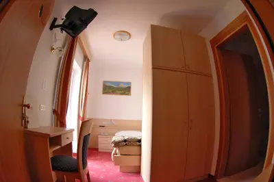 a room with a cabinet and a desk and a bedroom at Hotel Cristallo in Vigo di Fassa