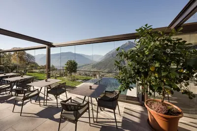a patio with tables and chairs and a view of mountains at Naturhotel Gruberhof in Schenna