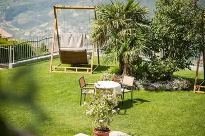 a garden with a table and chairs and a swing at Apartmenthaus Gruberhof in Schenna