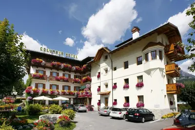 a large building with cars parked in a parking lot at Hotel Columbia & Spa in Cortina dʼAmpezzo