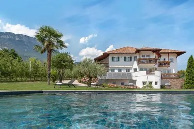 a villa with a swimming pool in front of a house at Mareithof Appartements Seeblick in Caldaro