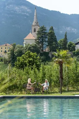 two women sitting on a bench next to a swimming pool at Mareithof Appartements Seeblick in Caldaro