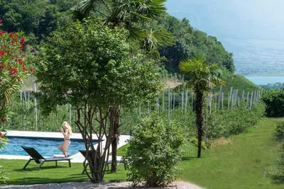 a woman is sitting in a chair next to a pool at Mareithof Appartements Seeblick in Caldaro