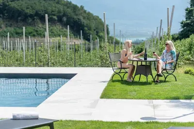two women sitting at a table next to a pool at Mareithof Appartements Seeblick in Caldaro
