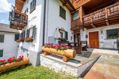 a house with red flowers in a courtyard at Apartments Berna in Ortisei
