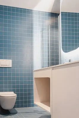 a blue tiled bathroom with a toilet and a mirror at Villa Kranebitt in Bressanone