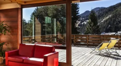 a living room with a red couch and chairs on a balcony at Hotel Club Regina E Fassa in Mazzin