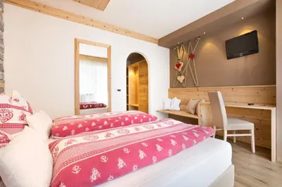 a bedroom with two beds and a desk at Hotel Azola in Canazei