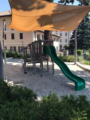 a playground with a green slide under an umbrella at Goldengel Design-Suiten Frieda Maria im Herzen von Kaltern in Caldaro