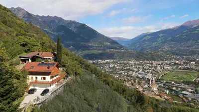 a house on the side of a mountain overlooking a town at Der Luemerhof in Marlengo