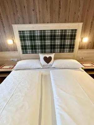 a large white bed with a heart pillow on it at Residence Ravisa Dolomites in Selva di Val Gardena
