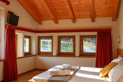 a bedroom with a bed with red curtains and windows at hotel Parco Pineta in Cavareno