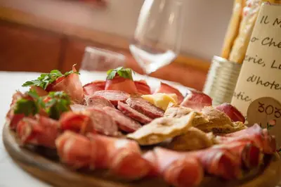 a plate of food with meat and a glass of wine at Romantic Charming Hotel Rancolin in Moena