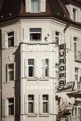 a bedroom with two beds and a chair and a window at Hotel Europa Splendid in Merano