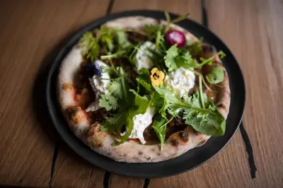 a pizza with greens on a black plate on a table at KRONE eat drink stay in Bressanone