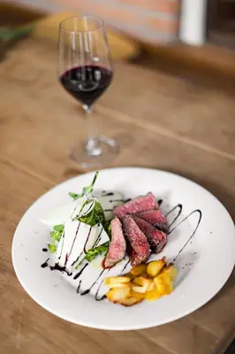 a white plate with meat and a glass of wine at KRONE eat drink stay in Bressanone