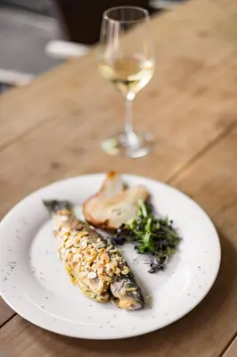 a white plate with fish and a glass of wine at KRONE eat drink stay in Bressanone