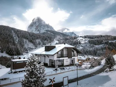 a house in the snow with a mountain in the background at Anna Lodges Dolomites in Santa Cristina in Val Gardena