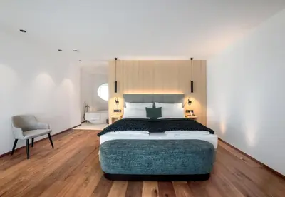 a bedroom with a large bed and a chair at Anna Lodges Dolomites in Santa Cristina in Val Gardena