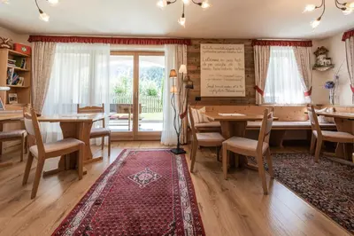 a dining room with wooden tables and chairs and a red rug at Les Gomines BB***** in San Vigilio Di Marebbe