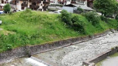 a river with a grassy hill next to a city at Cèsa Pier Sellaronda Dolomiti in Campitello di Fassa