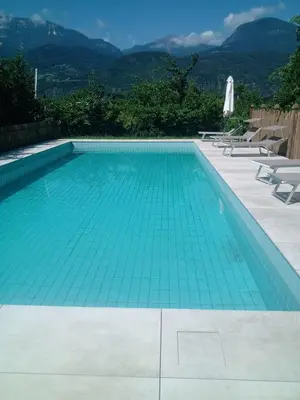 a swimming pool with blue water and chairs and mountains at Mittelbergerhof Ferienwohnungen in Vilpiano