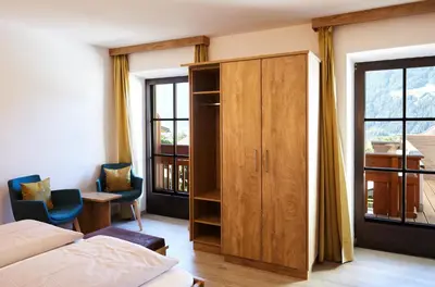 a bedroom with a bed and a cabinet and windows at Hotel Sonnenheim in Vipiteno
