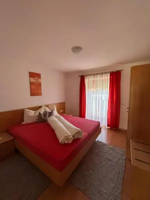 a bedroom with a bed with red sheets and a window at Appartements Schatzer in Valdaora