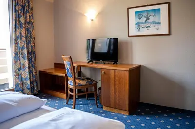 a hotel room with a desk with a tv and a bed at PanoramaHotel Penegal in Mendola