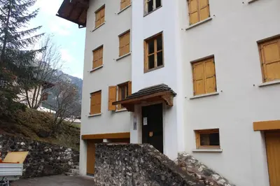 a white building with wooden windows and a stone wall at Cesa Monti pallidi 1 in Canazei