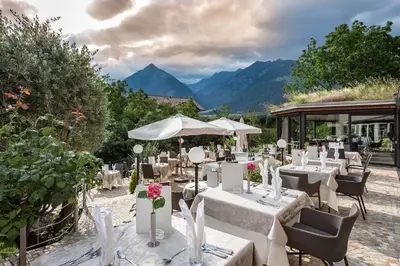 a restaurant with tables and chairs with mountains in the background at Baumgartner's Blumenhotel in Schenna