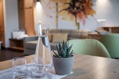 a vase and glasses on a table with a plant at Baumgartner's Blumenhotel in Schenna