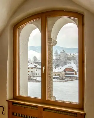 an arched window with a view of a snowy city at Krüglwirt in San Lorenzo di Sebato