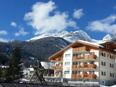 a hotel with snow covered mountains in the background at Residence Ciasa Alpe in Vigo di Fassa