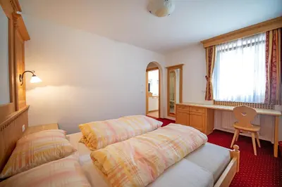 two beds in a room with a desk and a window at Apartments Berdan in Santa Cristina in Val Gardena