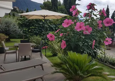 a patio with a table and umbrella and pink flowers at Appartements Dornach in Schenna
