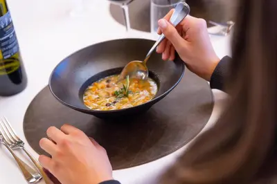 a woman is eating a bowl of food with a spoon at Hotel Meida in Pozza di Fassa