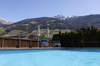 two chairs and a swimming pool with mountains in the background at Pension Kleon in Rifiano
