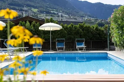 a swimming pool with chairs and an umbrella at Pension Kleon in Rifiano