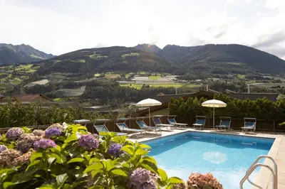 a swimming pool with chairs and umbrellas and mountains at Pension Kleon in Rifiano