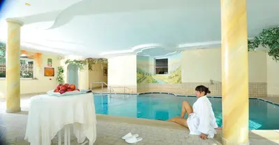 a woman sitting at a table next to a swimming pool at Hotel Sonnenheim in Avelengo